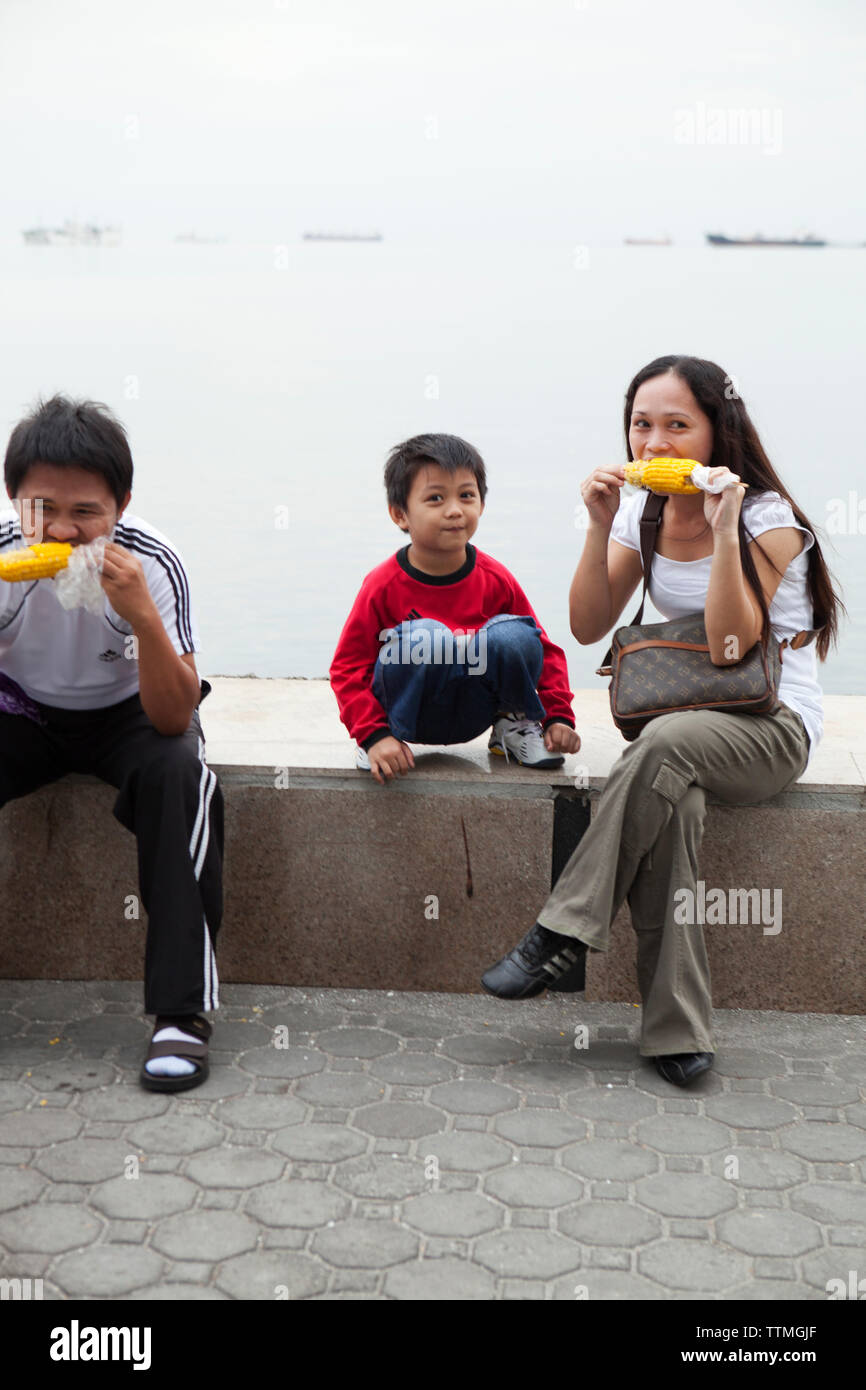 Filipinas, Manila, la familia goza de algunas plantaciones de maíz en el Rojas Blvd Paseo de la Bahía Foto de stock