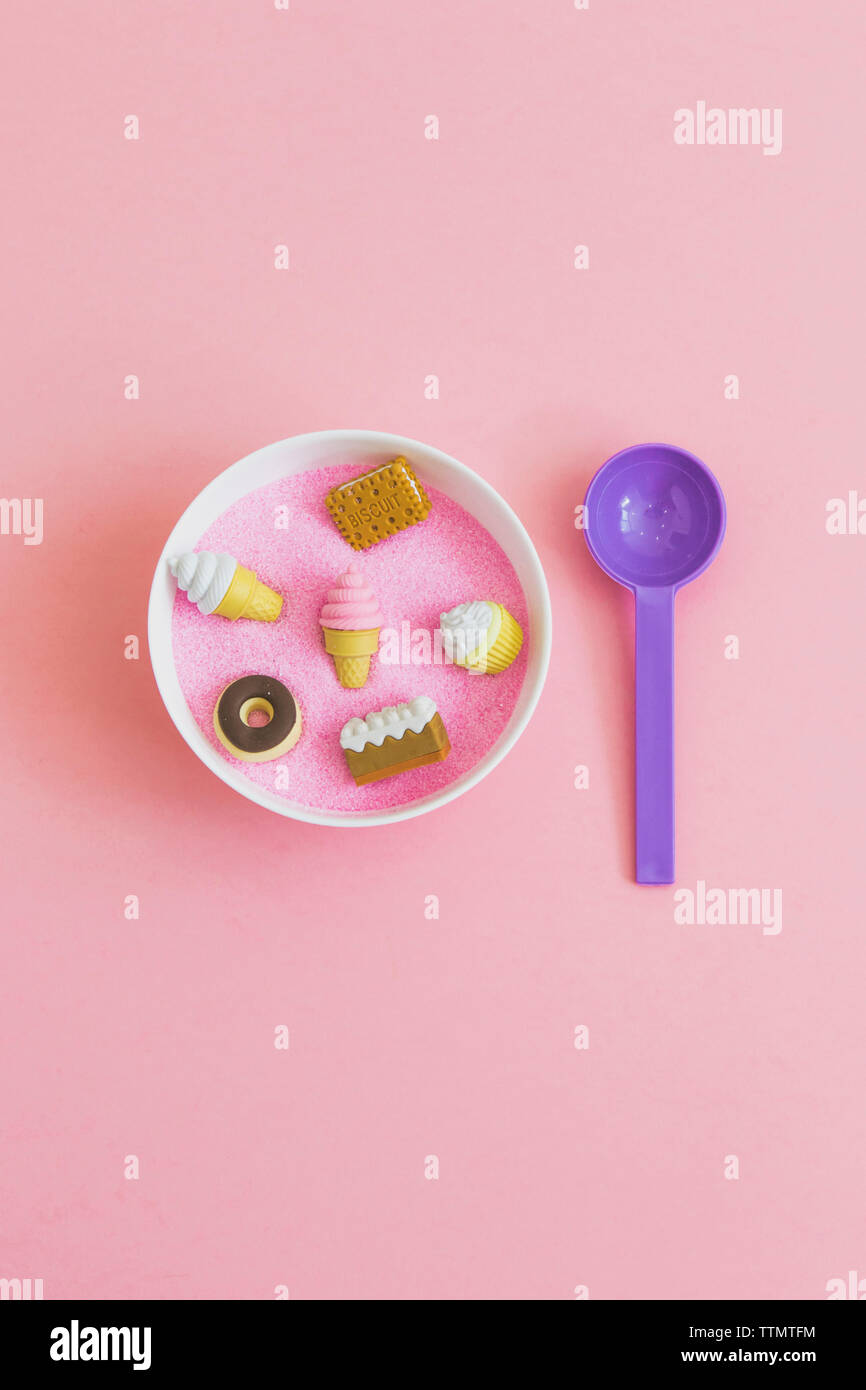 Vista aérea de diversos alimentos dulces juguetes en un tazón con una cuchara sobre fondo de color rosa Foto de stock