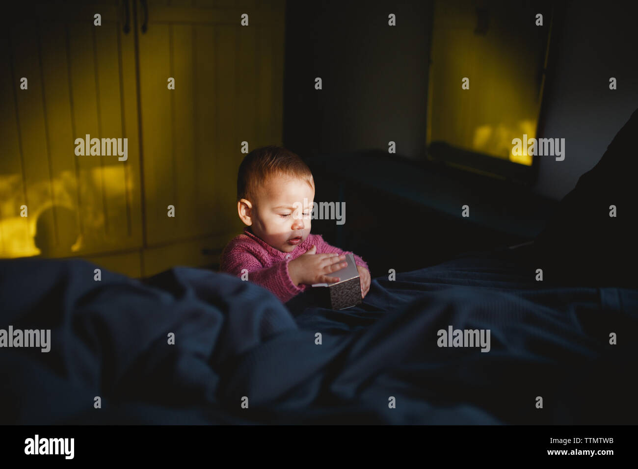 Una niña jugando con una caja de cartón en la cima de la cama Foto de stock