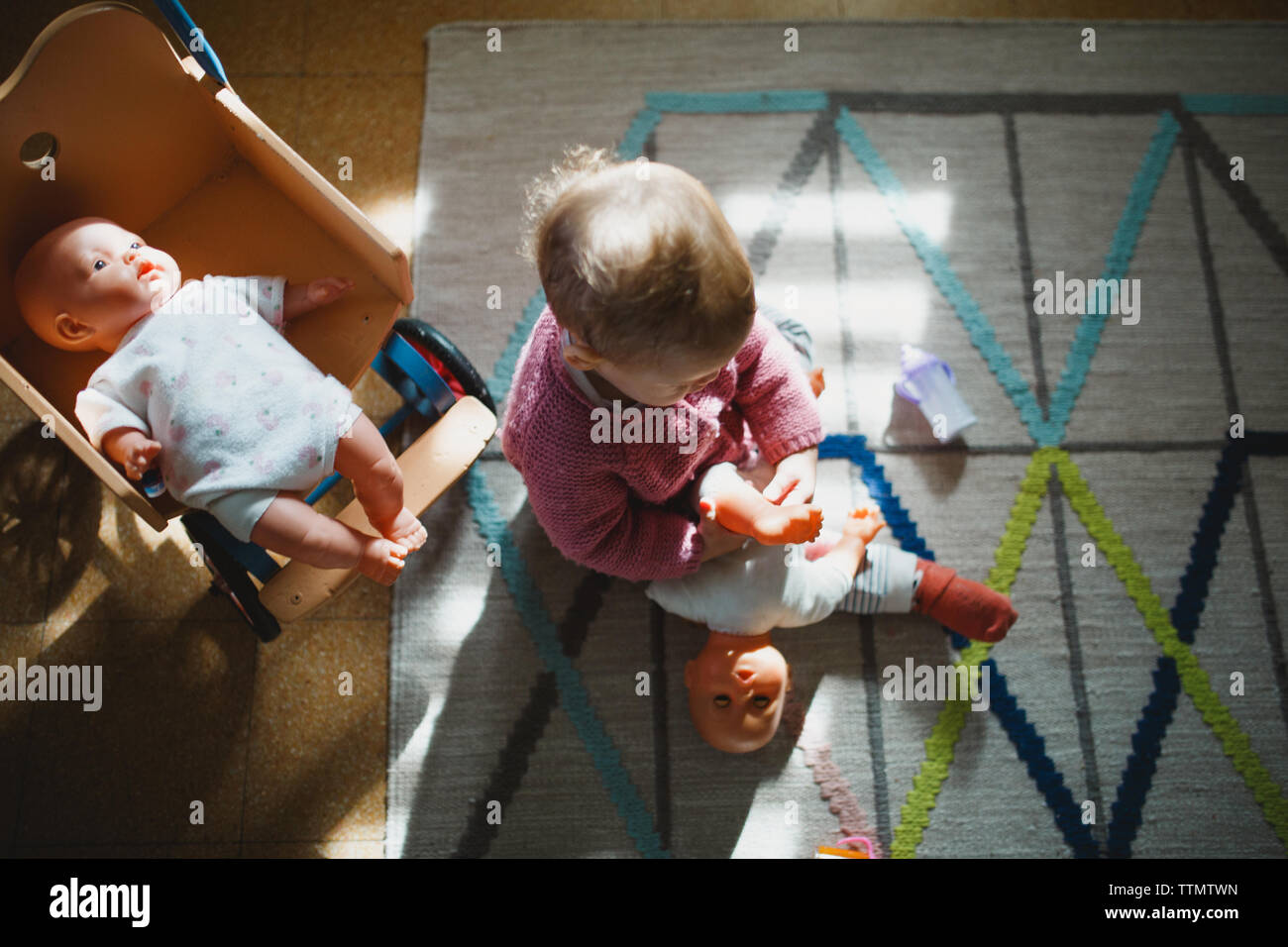 Una niña sentada sobre una alfombra de jugar con sus muñecas Foto de stock
