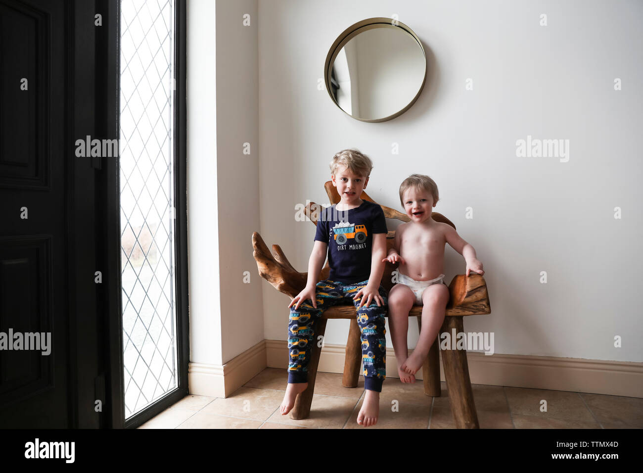 Pajama Clad Hermanos sentados en banco de madera orgánicos junto a la ventana Foto de stock