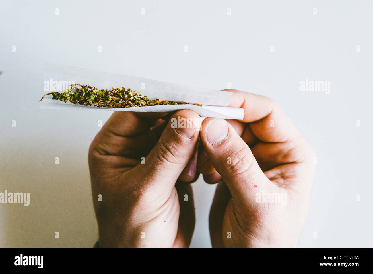Recorta las manos del hombre rolling marihuana juntas en papel sobre tabla blanca en casa Foto de stock