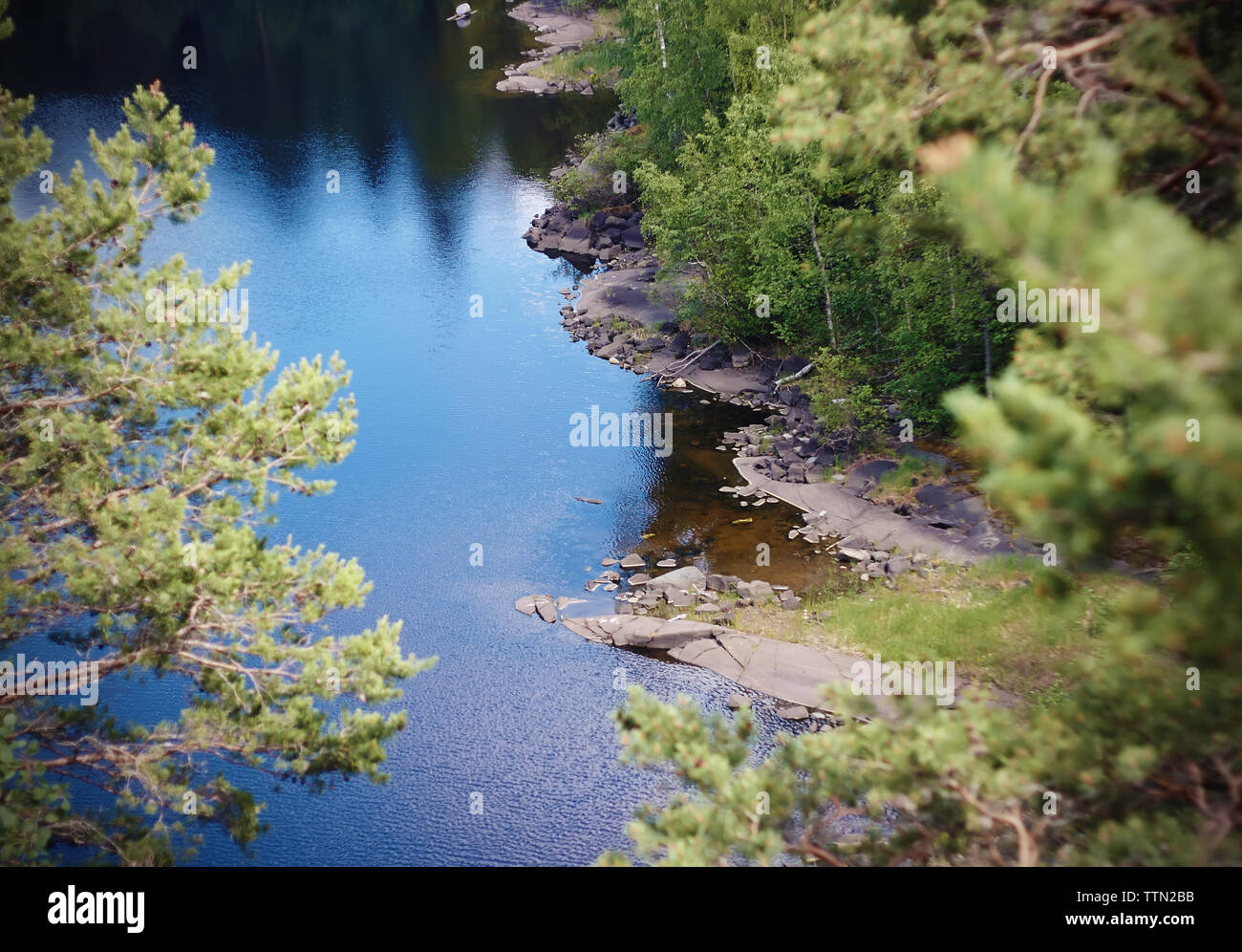 Bosque limpio lago entre las costas rocosas, reflejando el azul del cielo, cubiertos con pequeñas ondulaciones. Foto de stock