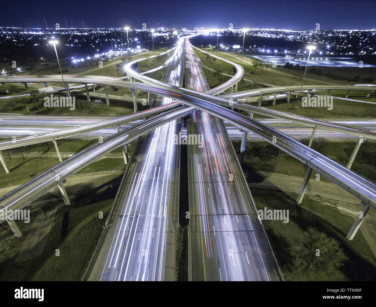 Vista aérea de estelas de luz en intersecciones de la carretera en la ciudad iluminada por la noche Foto de stock