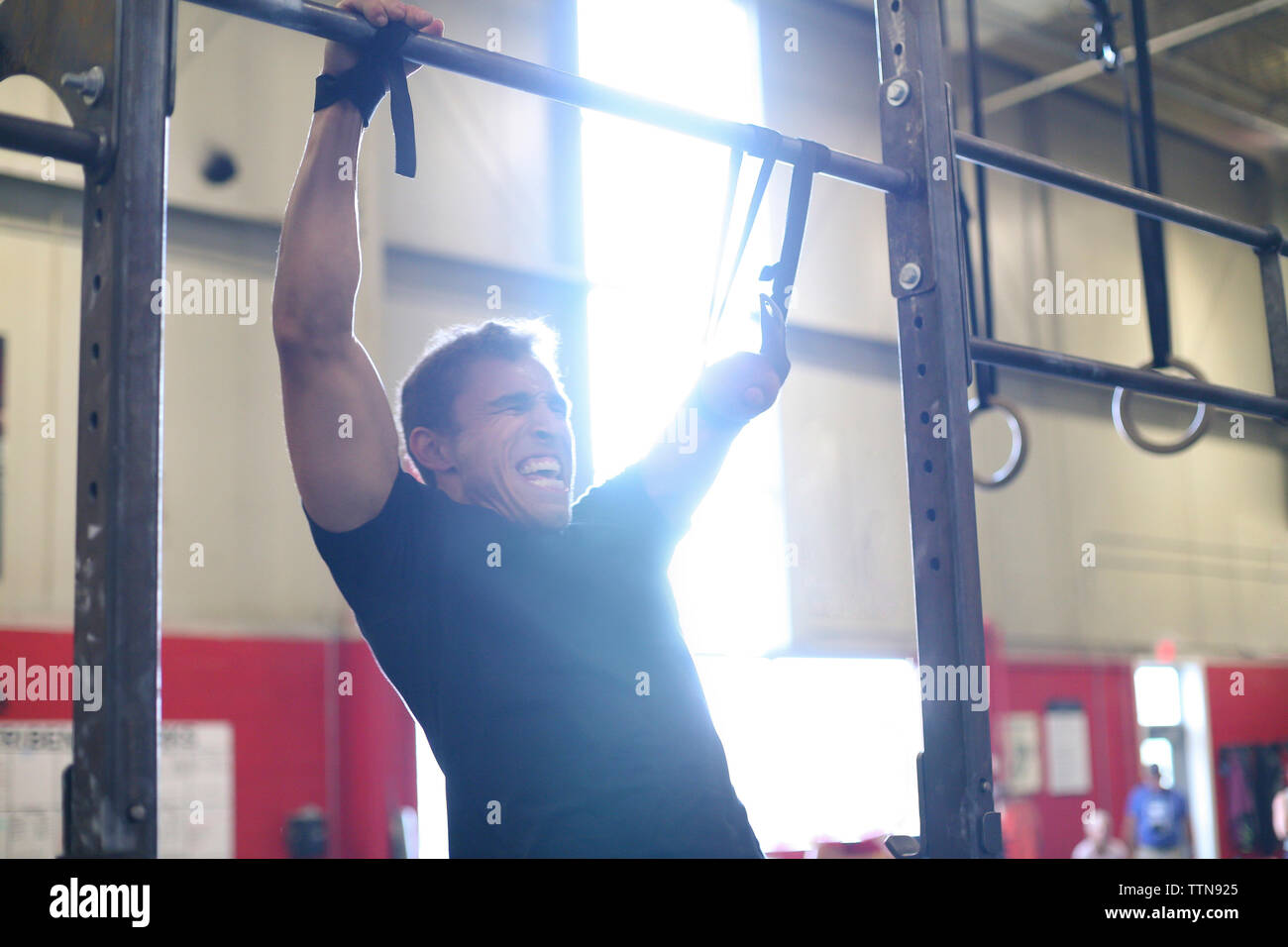 Adaptive atleta masculino agresivo gritando mientras hacen chin-ups en el gimnasio Foto de stock