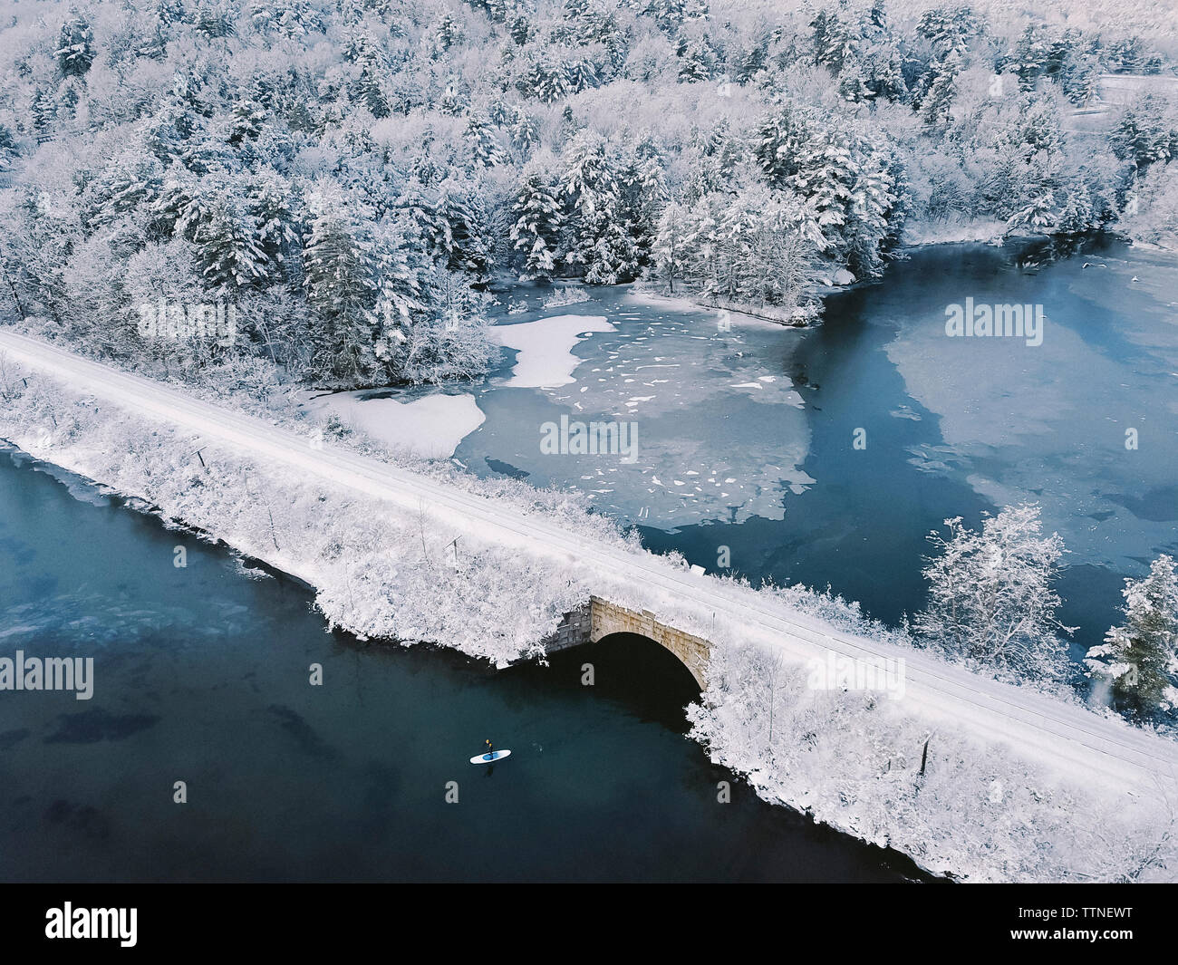Un alto ángulo de visualización de la persona paddleboarding en el lago por el puente durante el invierno Foto de stock