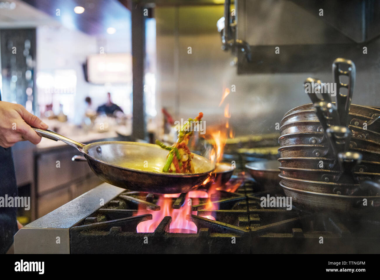 Imagen recortada del chef echar las verduras en la sartén en la cocina comercial Foto de stock