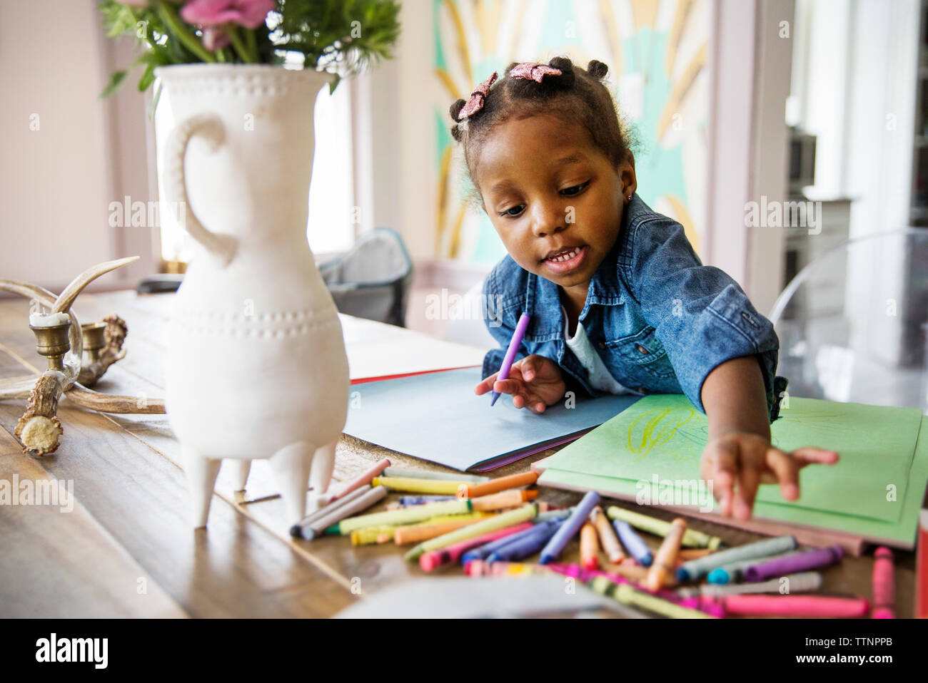 Linda niña alcanzando lápices de colores sobre la mesa en casa Foto de stock