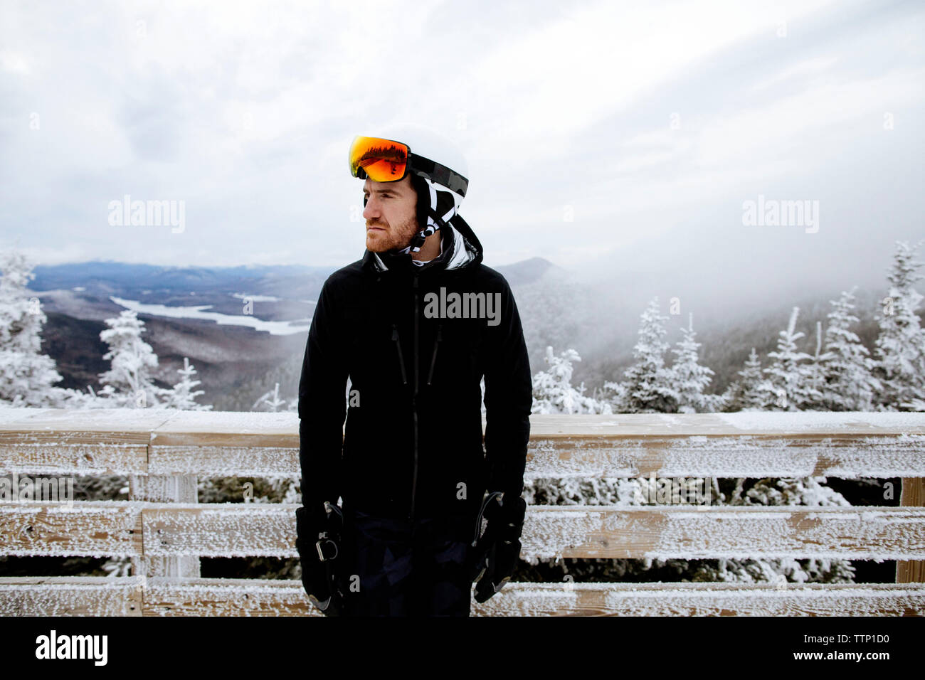 Pensativo hombre vestido con ropa de esquí mientras está de pie contra la  valla de madera congelada durante la niebla Fotografía de stock - Alamy
