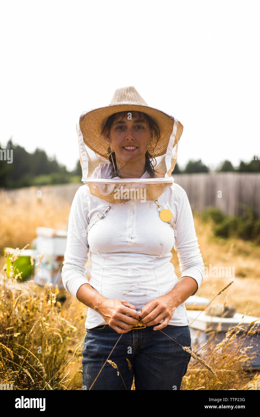 Retrato de apicultor vistiendo máscara protectora y hat estando de pie en el campo contra el cielo claro Foto de stock