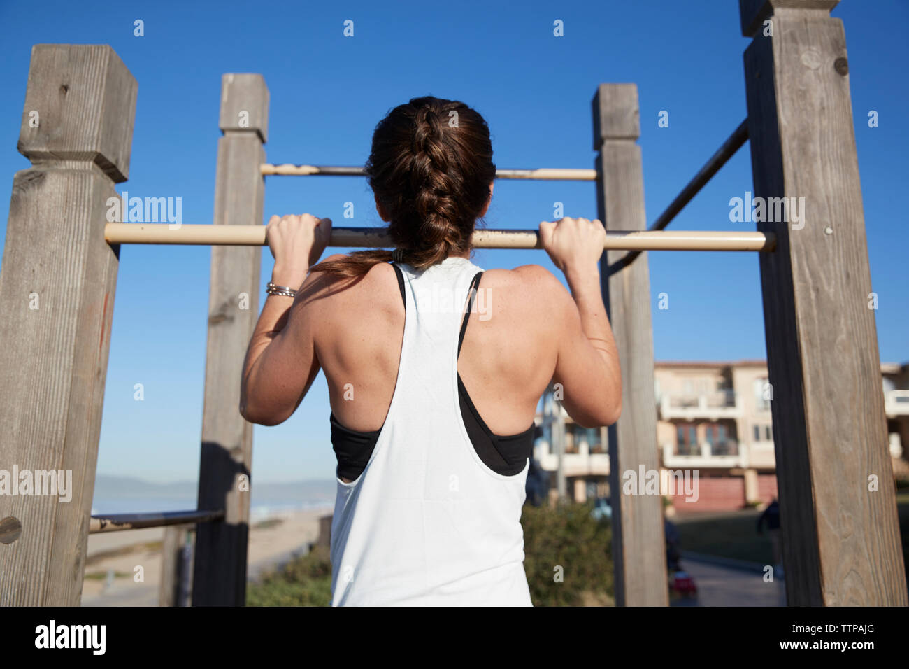 Vista trasera de la mujer haciendo chin-ups en la barra de gimnasia en la playa Foto de stock