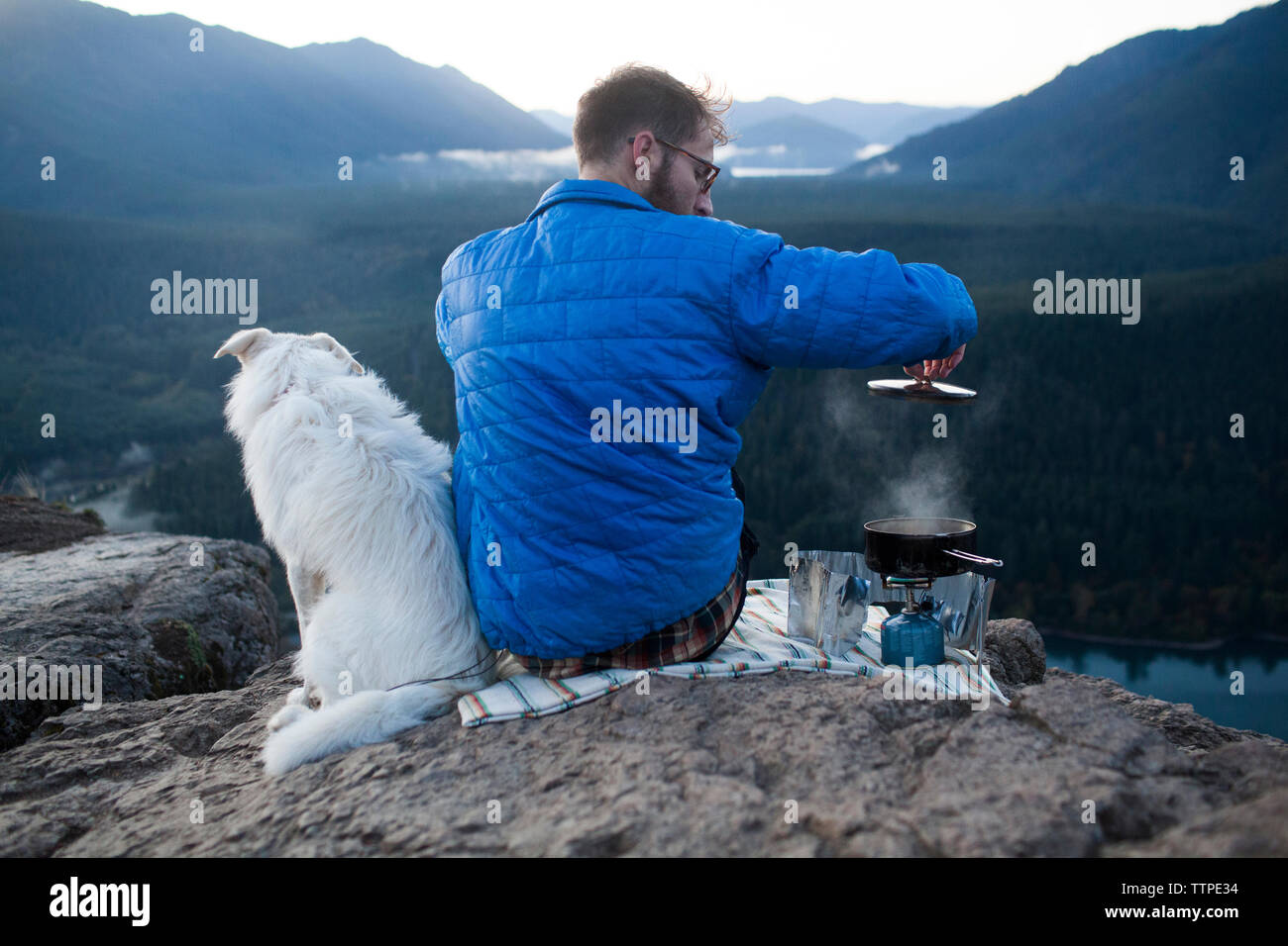 Vista trasera del hombre con el perro la cocción de los alimentos en las montañas Foto de stock