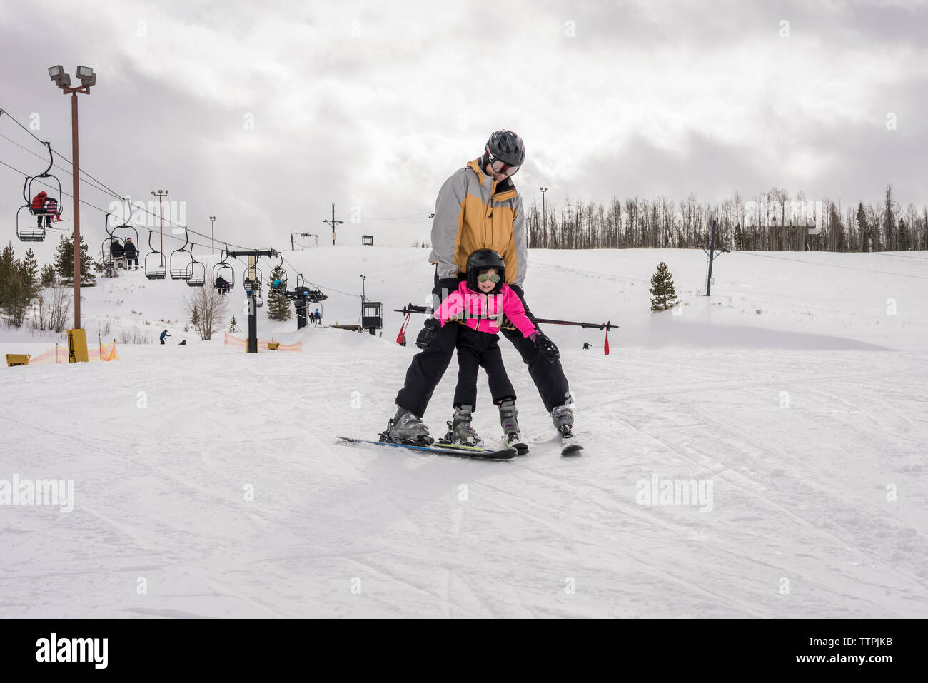 Padre con hija esquiando en paisaje cubierto de nieve contra el cielo nublado Foto de stock