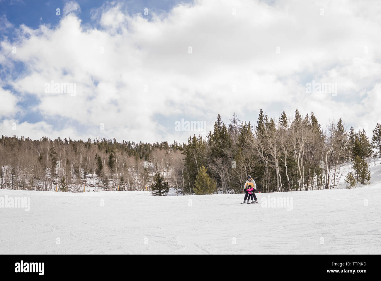 Padre con hija esquiando en paisaje cubierto de nieve contra el cielo nublado en el bosque Foto de stock