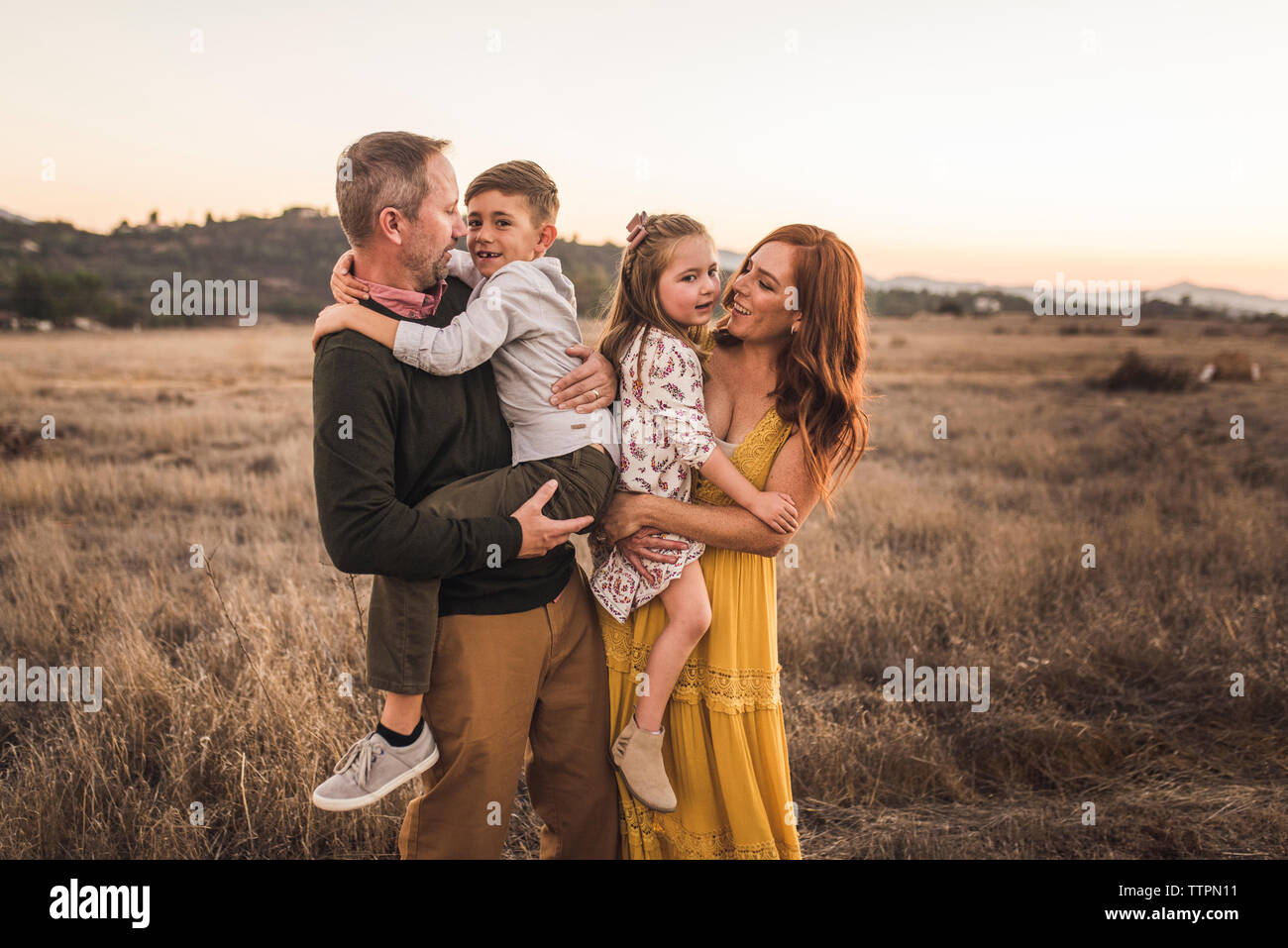 Chico y chica celebrado por sus padres en el campo de California durante la puesta de sol Foto de stock