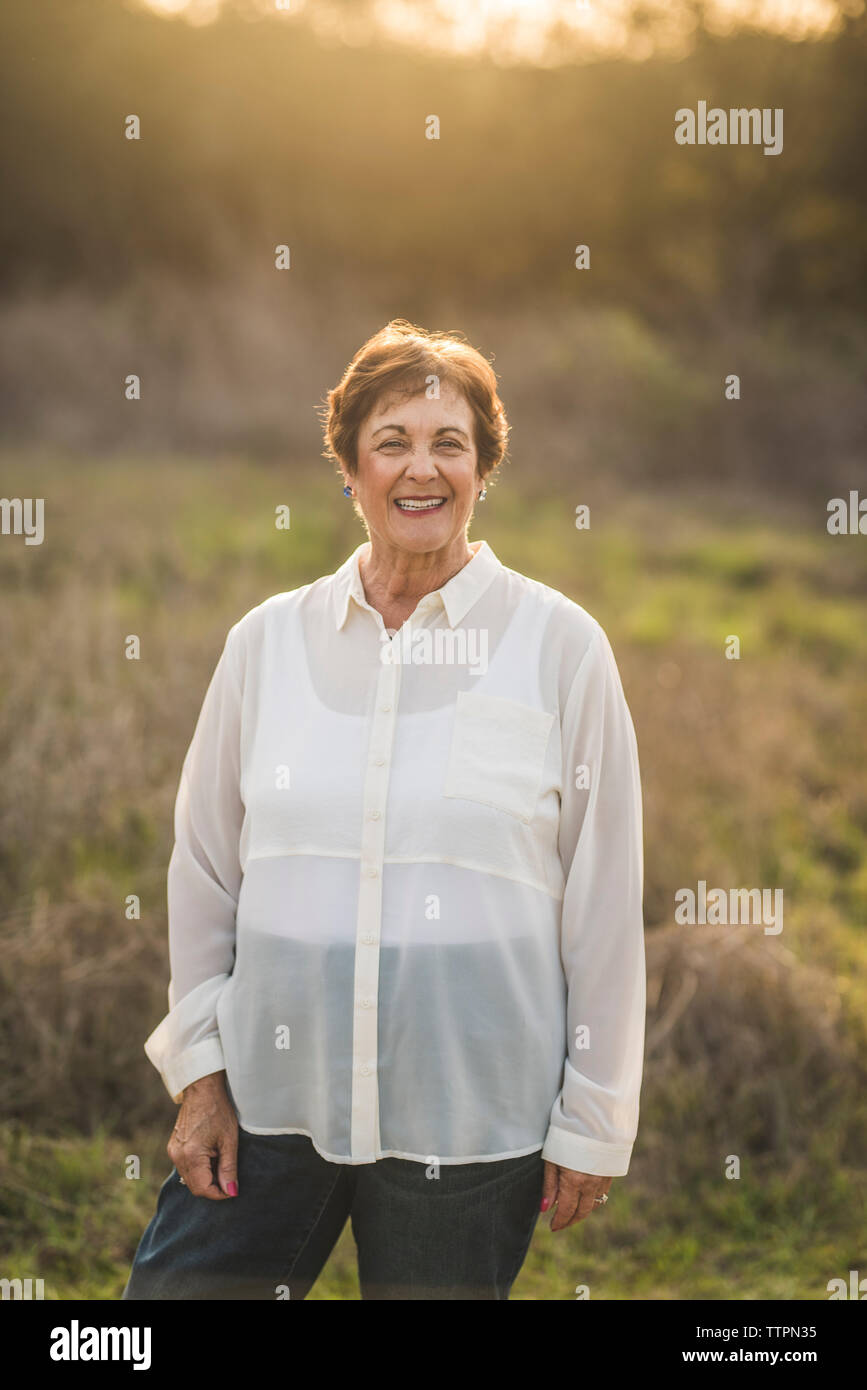 Retrato de mujer sonriente senior en la cámara en el campo retroiluminado Foto de stock