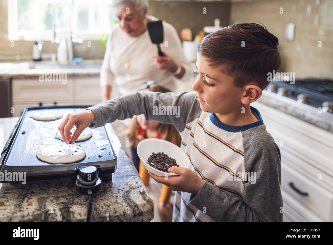 Joven cocina tortitas con familia multigeneracionales Foto de stock