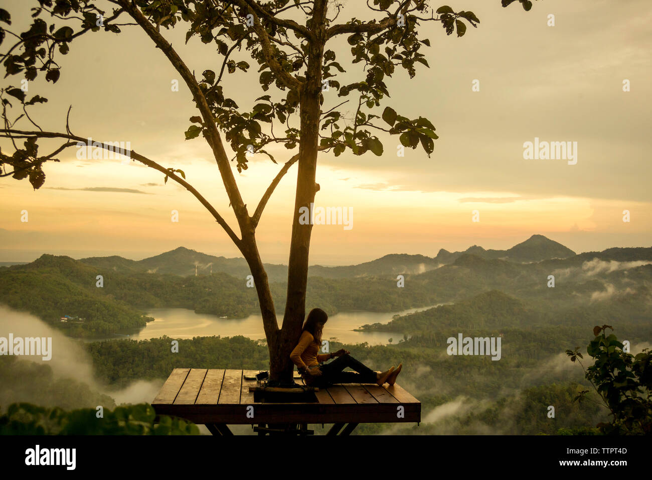 Mujer relajante mientras está sentado en el puesto de observación durante la puesta de sol Foto de stock