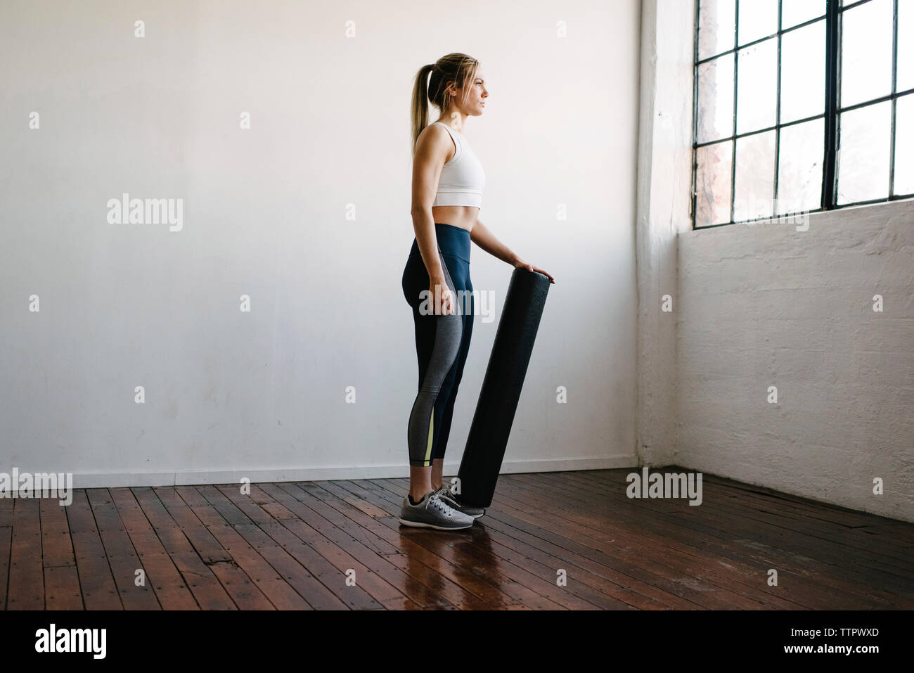 Vista lateral de la mujer sosteniendo equipos para hacer ejercicio mientras está parado en el gimnasio Foto de stock