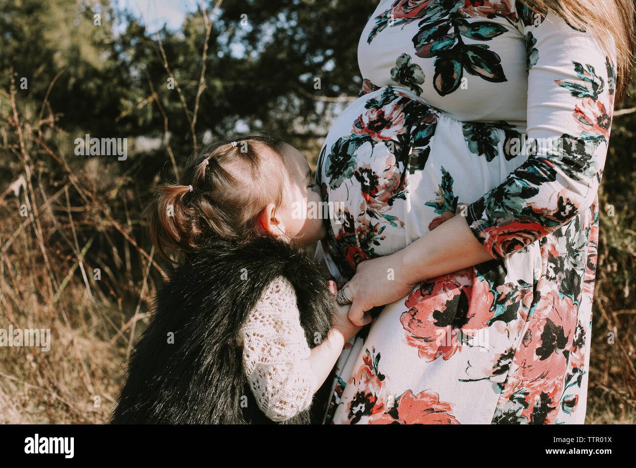 Besos hija amorosa del vientre de la madre embarazada mientras está de pie en el bosque Foto de stock