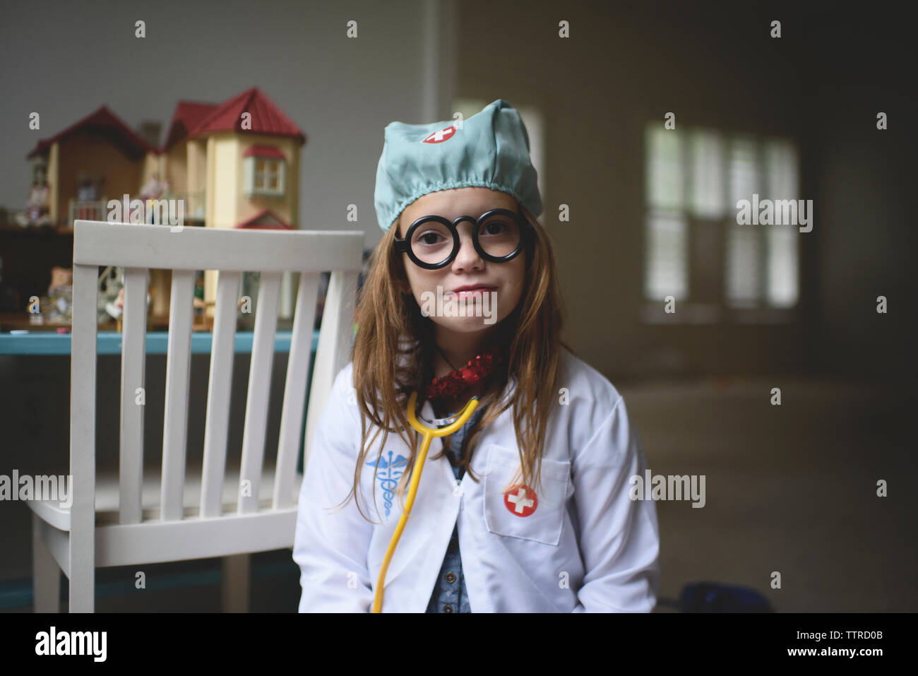 Retrato de linda chica en traje del doctor sentado en casa Foto de stock