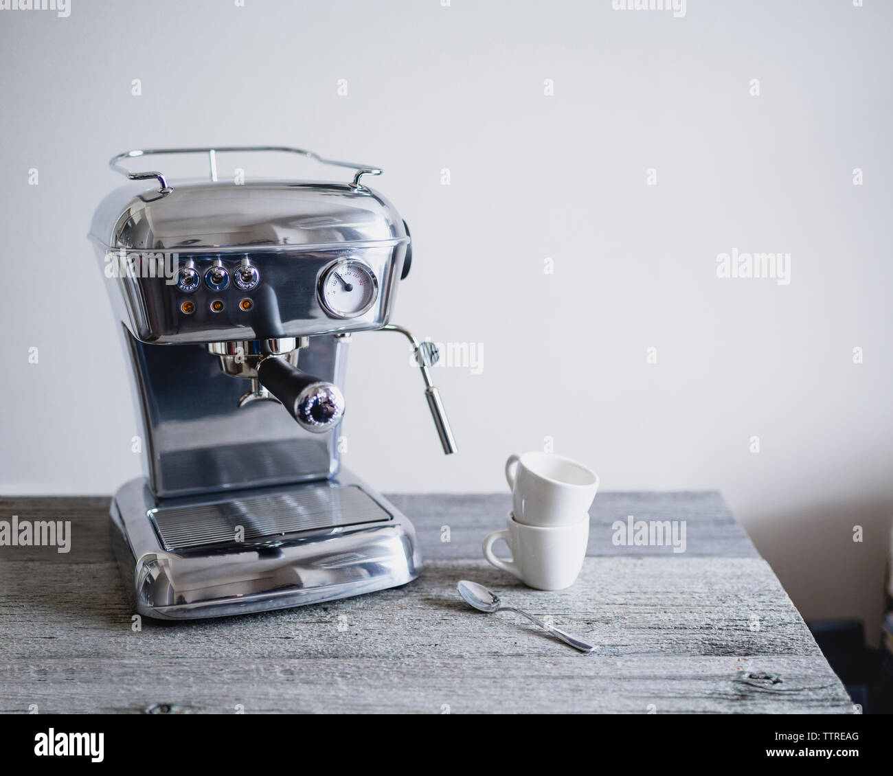 Máquina de café espresso con las tazas de café y cuchara en la tabla Foto de stock