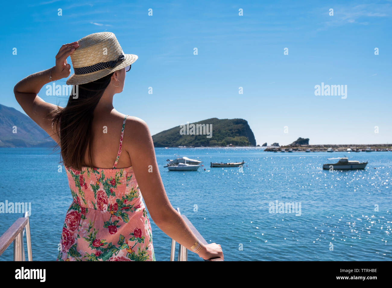 Vista trasera de una mujer mirando el mar mientras está de pie en el barco contra el cielo azul durante el día soleado Foto de stock