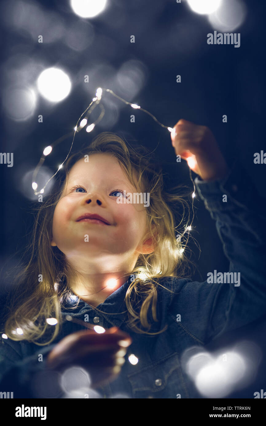 Feliz niña jugando con las luces de la cadena iluminada durante la noche Foto de stock