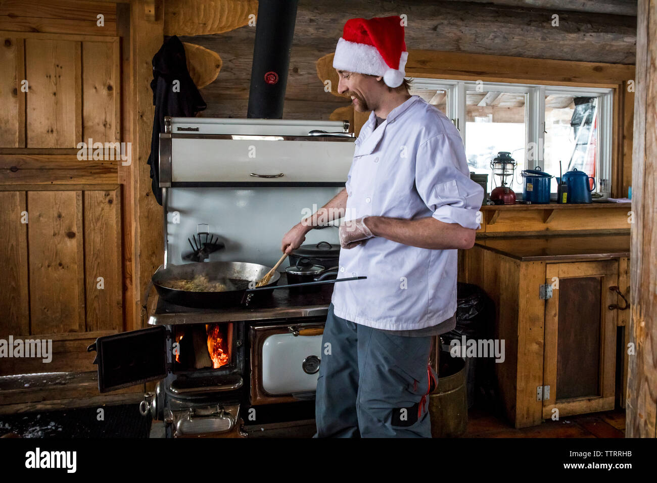 Un hombre con un sombrero de Navidad cocineros desayuno sobre una estufa de  leña en una cabaña de montaña para motonieve invitados a disfrutar de un  día de invierno Fotografía de stock -