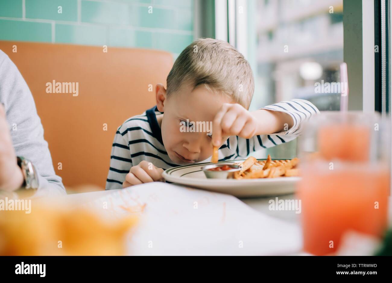 Joven comiendo papas fritas se sumerge en salsa en un restaurante Foto de stock