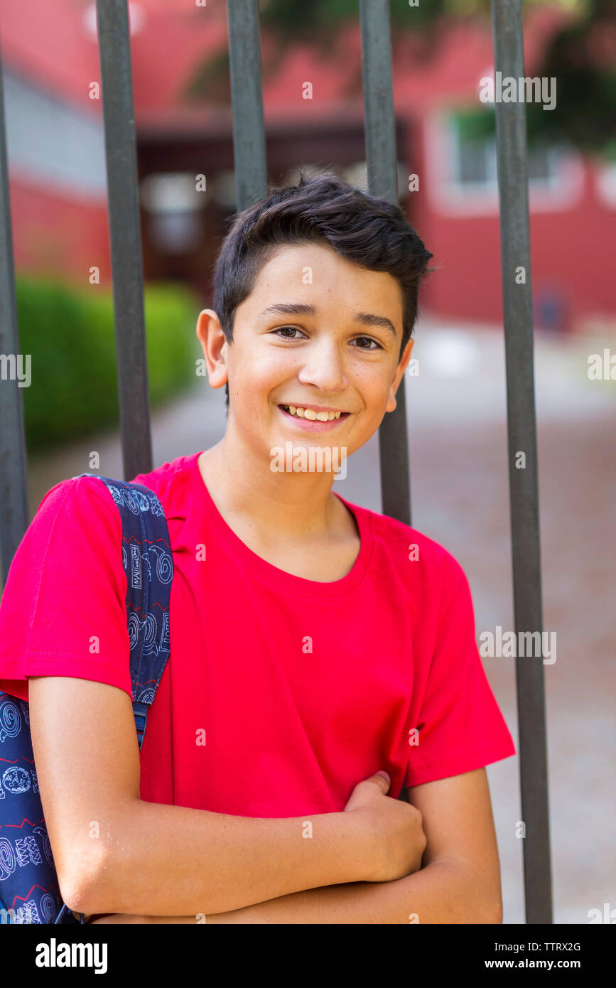 Retrato de sonriente colegial con mochila de pie en la puerta contra el edificio escolar Foto de stock