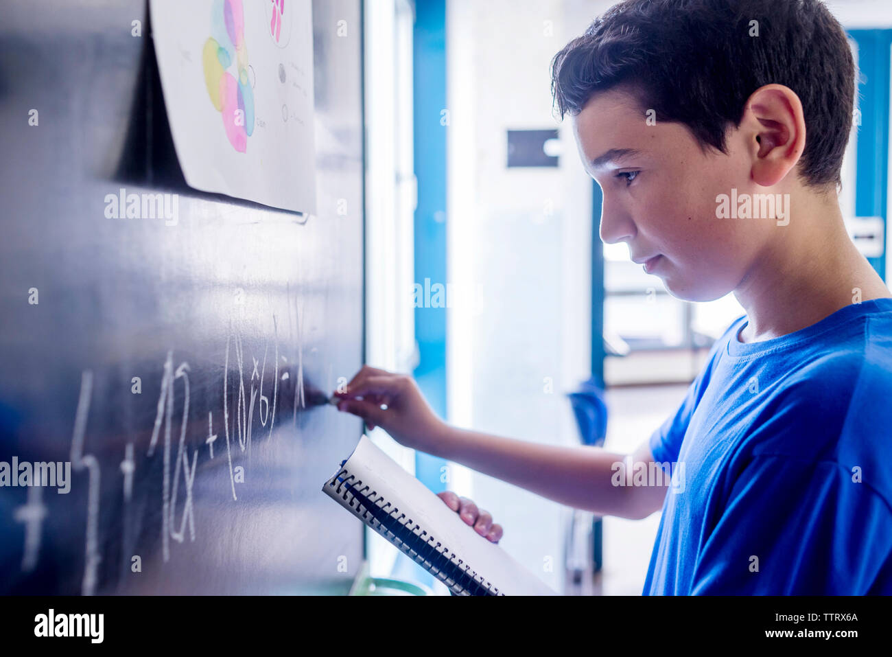 Vista lateral del colegial practicando matemáticas en la pizarra en el aula Foto de stock