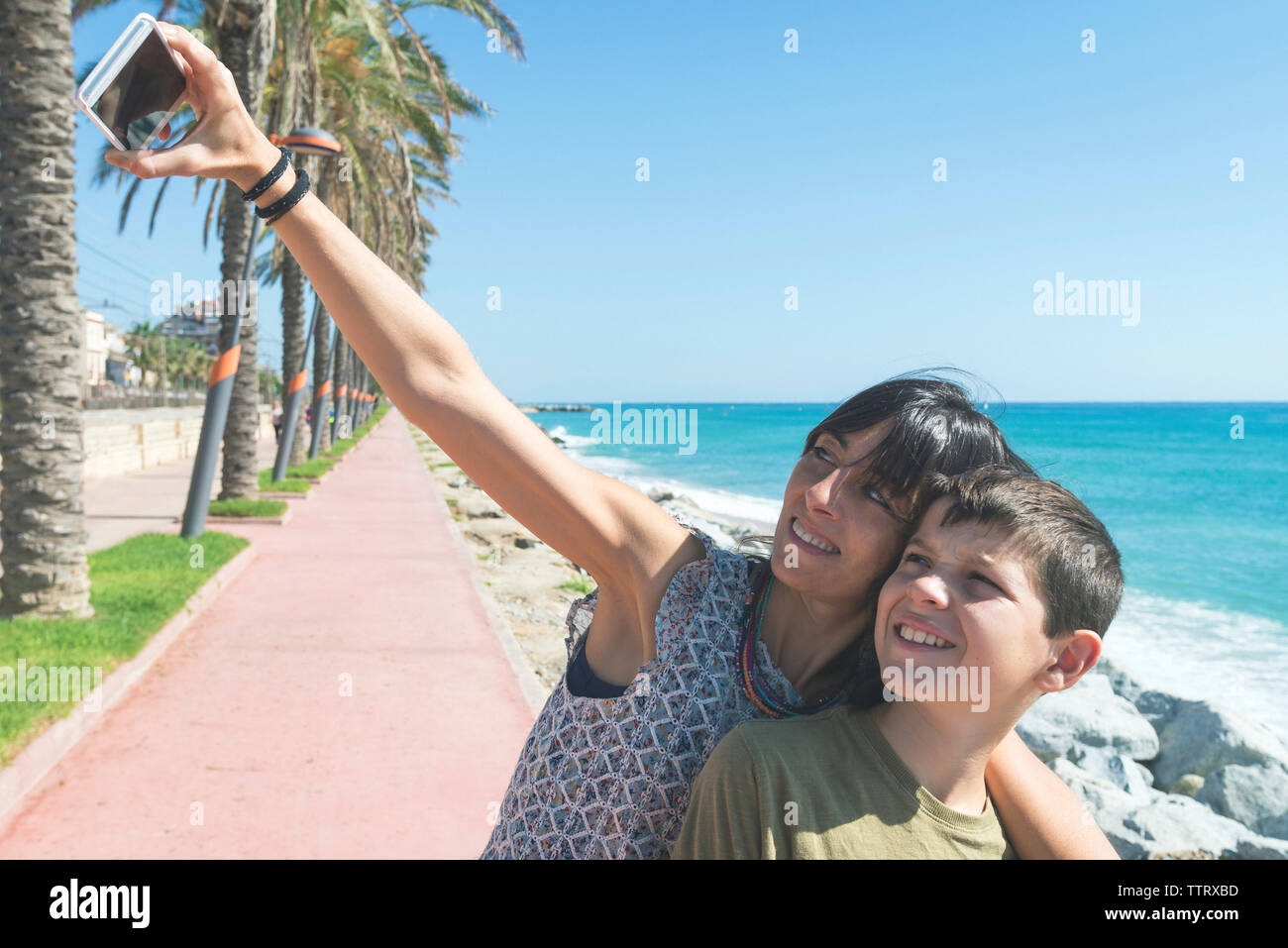 Madre e hijo de pie junto a la playa mientras toma un selfie Foto de stock