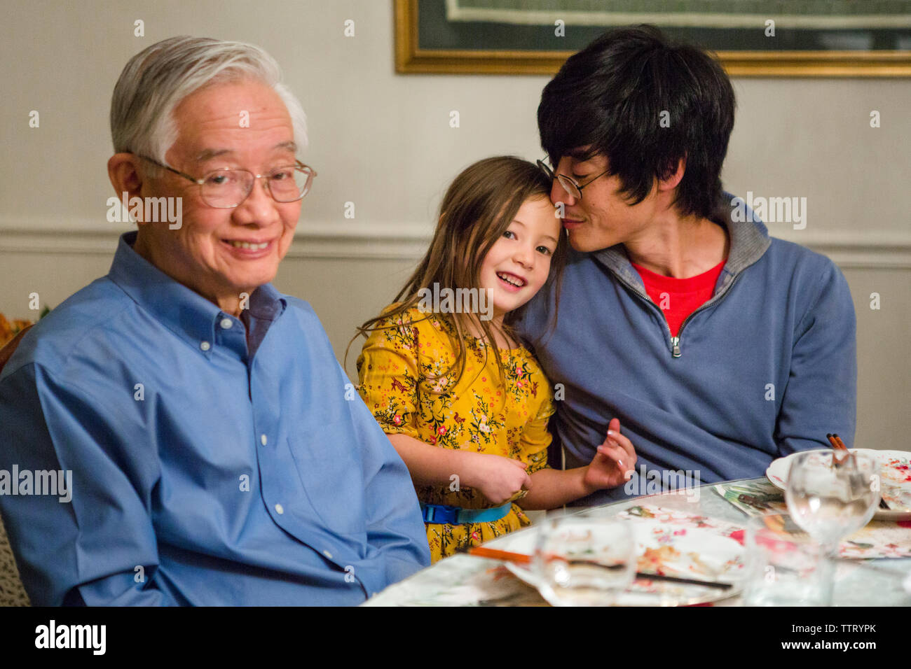 Una linda niña está con su padre y su abuelo en la mesa Foto de stock