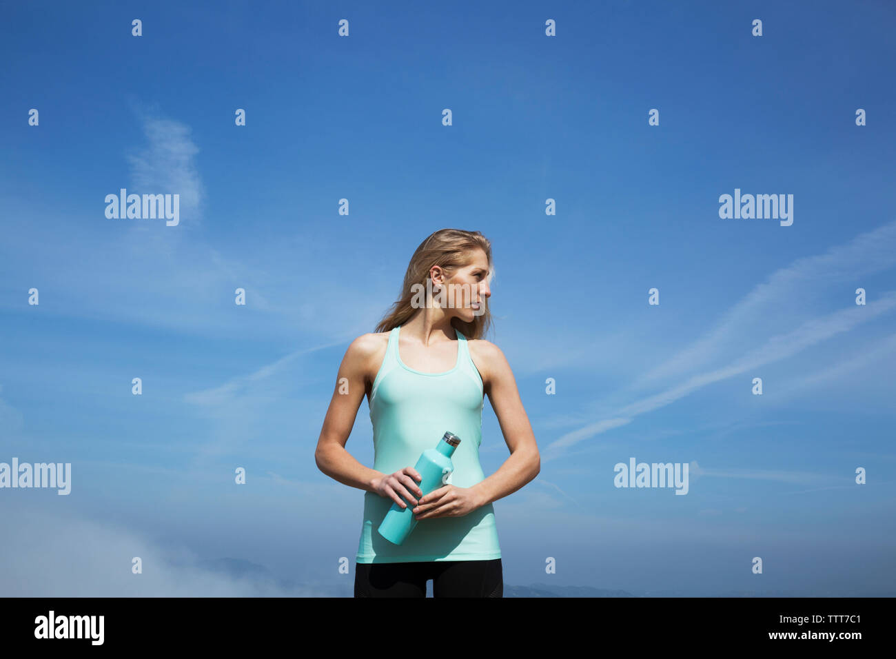 Mujer sosteniendo botella mirando a otro lado mientras está de pie contra el cielo Foto de stock