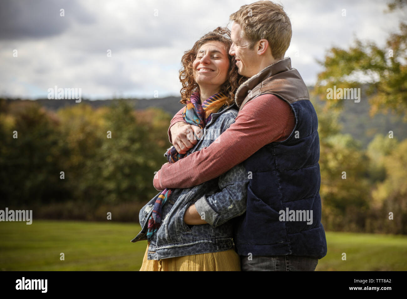 Pareja abrazada en abrazo sonriendo y riendo con los ojos cerrados en el campo Foto de stock