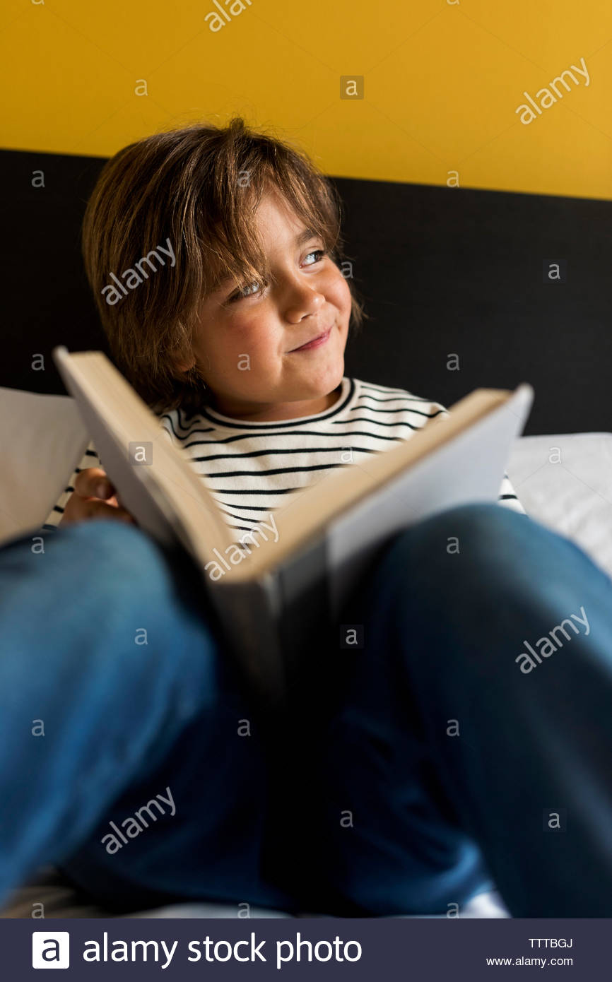 Joven en un dormitorio amarillo leyendo un libro en la cama Foto de stock