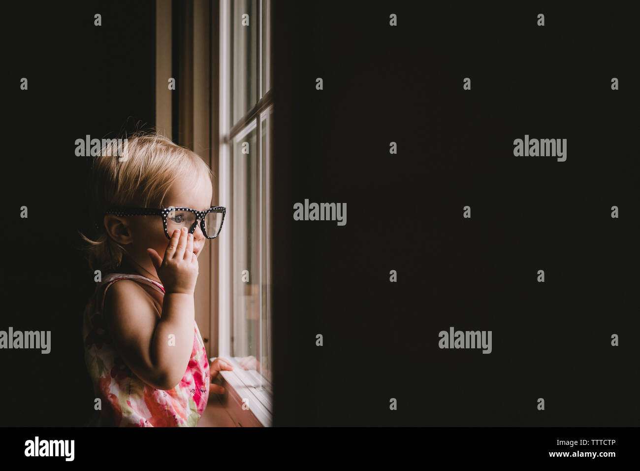 Baby Girl el uso de anteojos mientras busca a través de la ventana Foto de stock