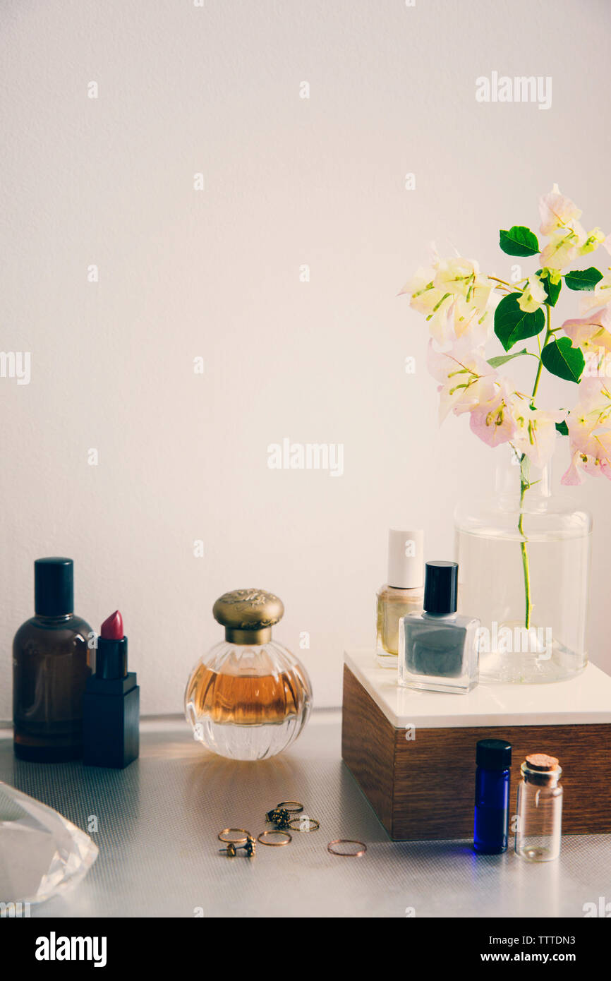 Productos de belleza con joyas y florero en la mesa contra la pared blanca Foto de stock