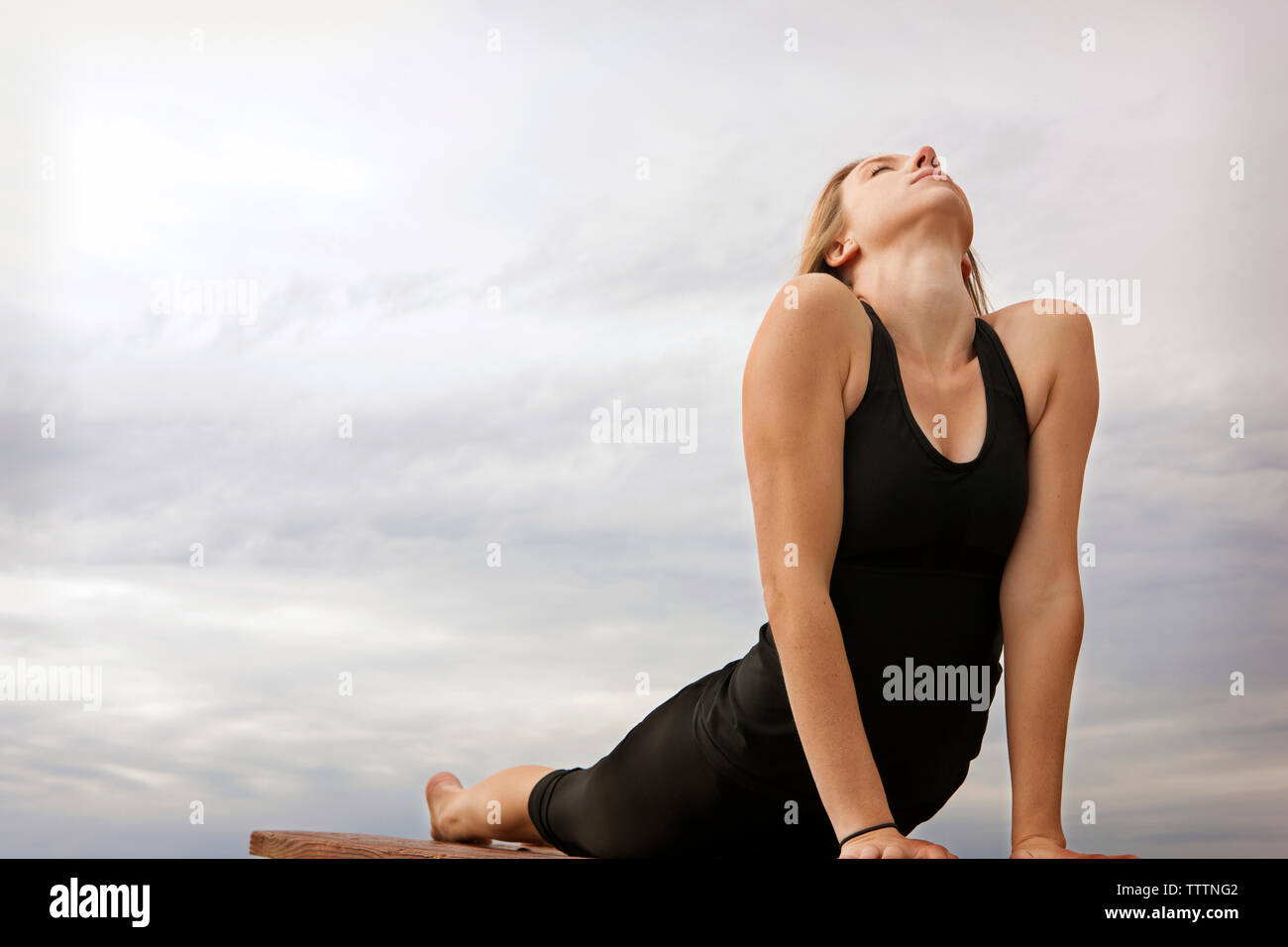 Mujer joven practicando yoga pose perro boca arriba contra el cielo nublado Foto de stock