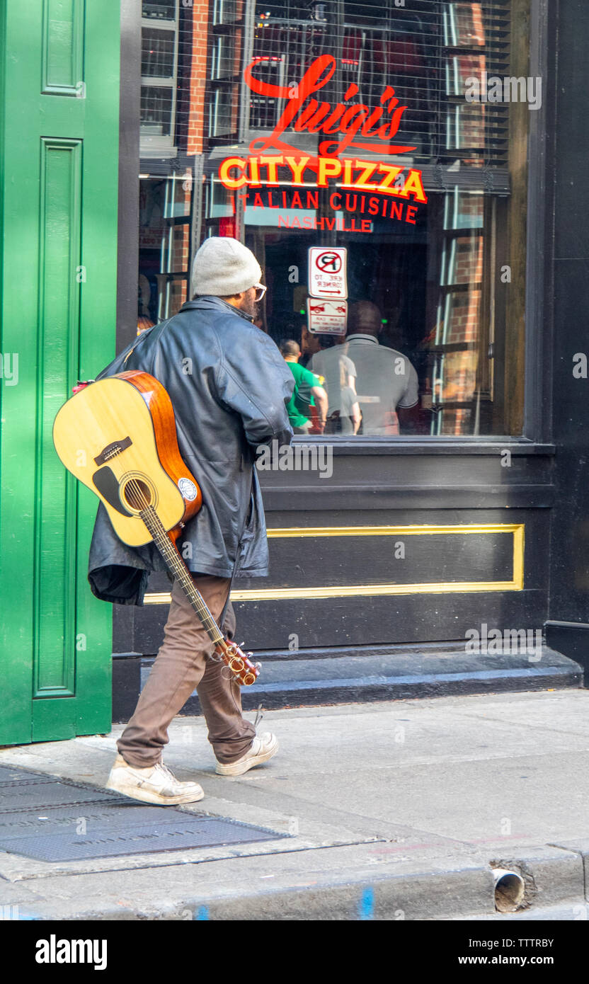 Músico callejero con una guitarra acústica, pasando por la ciudad de Luigi's Pizza Restaurant en 3rd Ave de Nashville, Tennessee, EE.UU.. Foto de stock