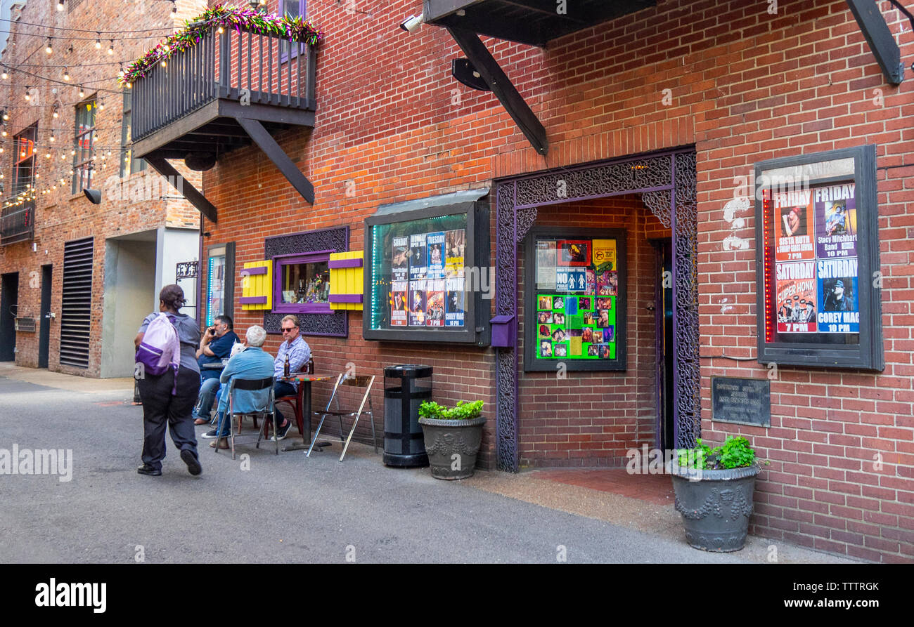 Una mujer caminando, y tres hombres sentados en una mesa fuera de Bourbon Street Blues y el Boogie Bar en impresoras Alley de Nashville, Tennessee, EE.UU.. Foto de stock