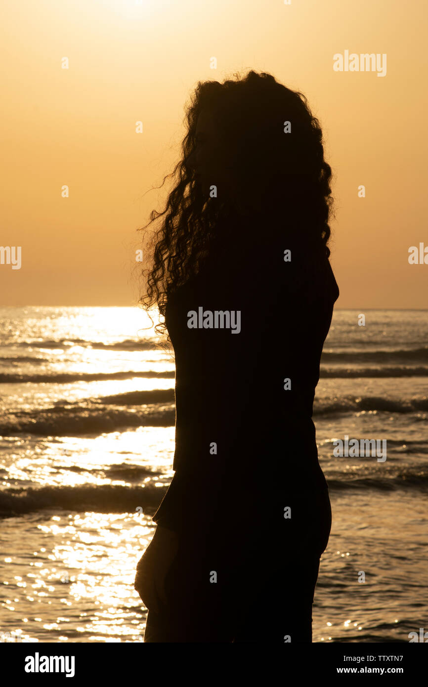 Vista lateral de la silueta de la mujer joven en la playa en el atardecer. Foto de stock