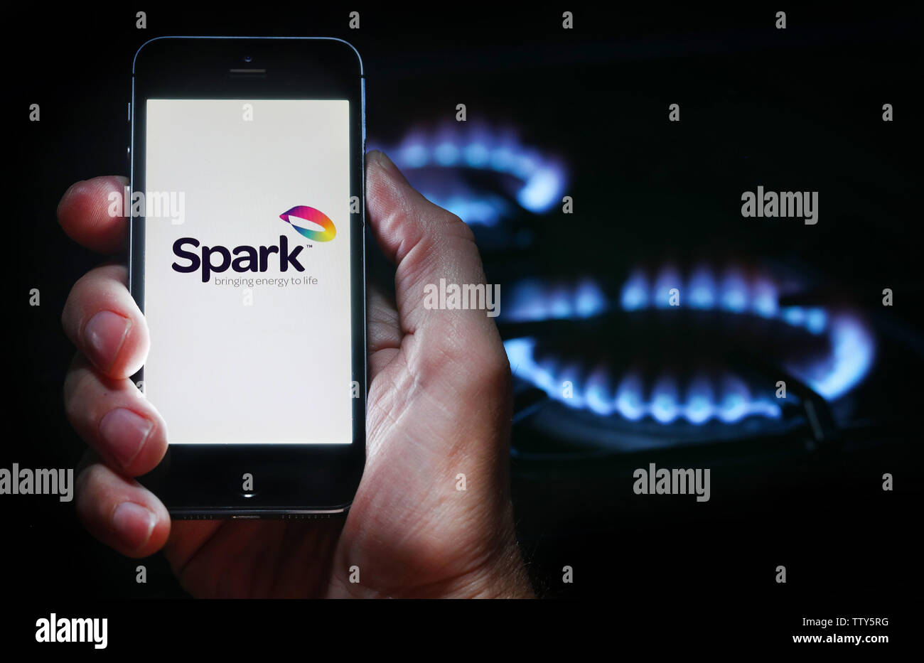 Un hombre mirando el logotipo del sitio web de la compañía de energía chispa en su teléfono en frente de su cocina de gas (uso editorial solamente) Foto de stock