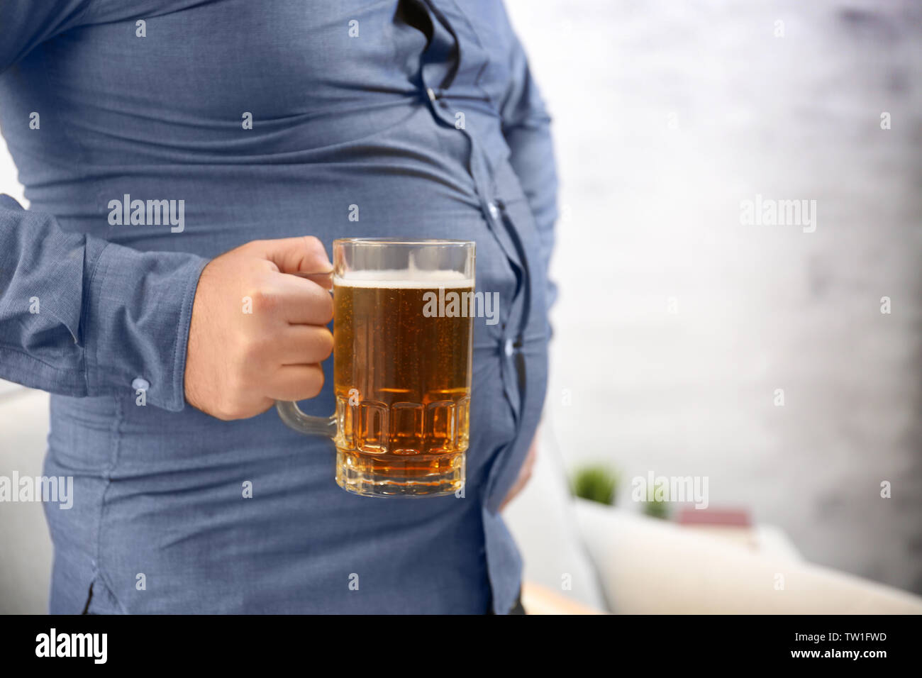 Hombre con gran celebración del vientre vaso de cerveza en casa Fotografía  de stock - Alamy