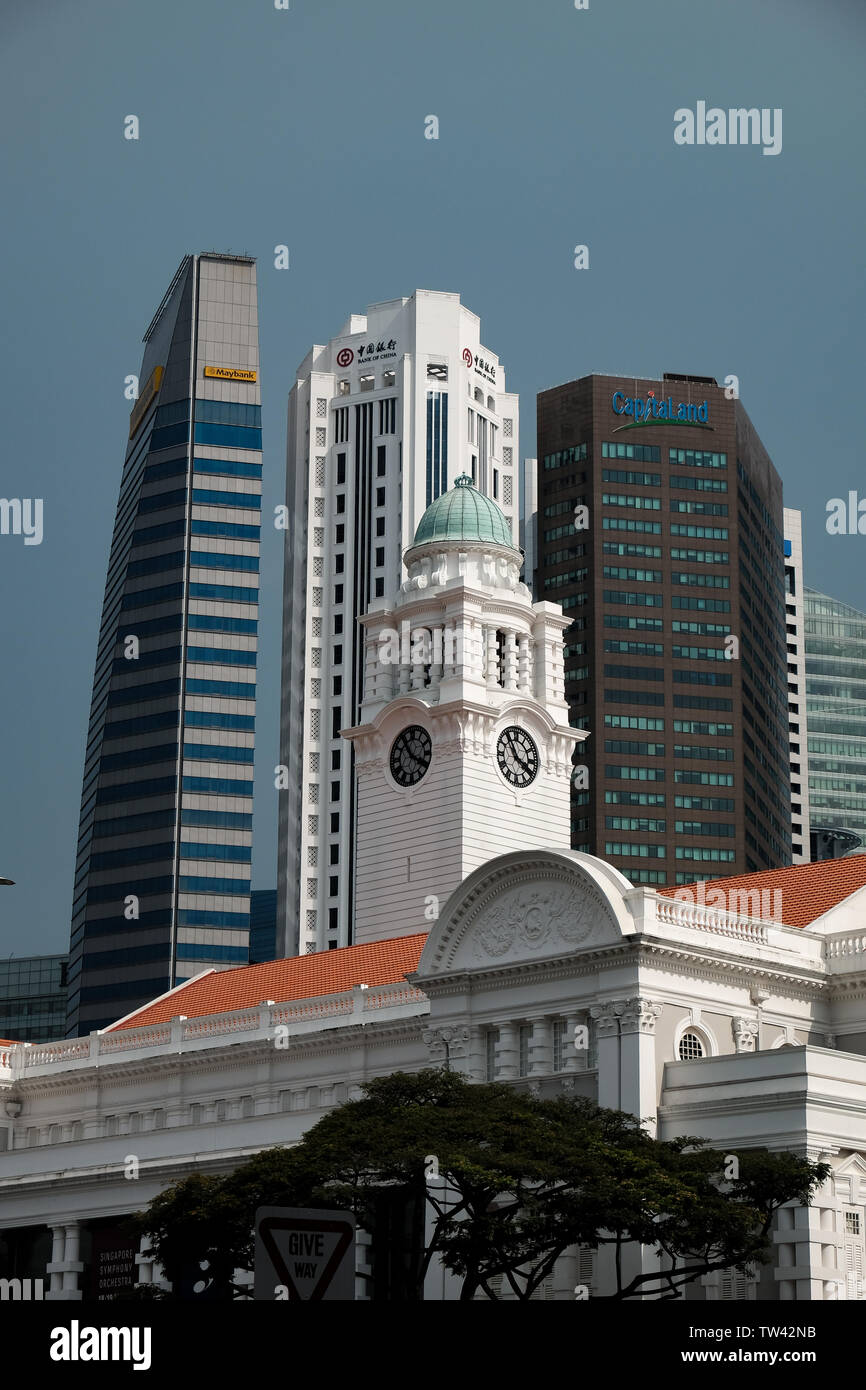 Un paisaje urbano vista de la torre del reloj del Teatro Victoria y la sala de conciertos con los rascacielos del distrito financiero de Singapur detrás Foto de stock