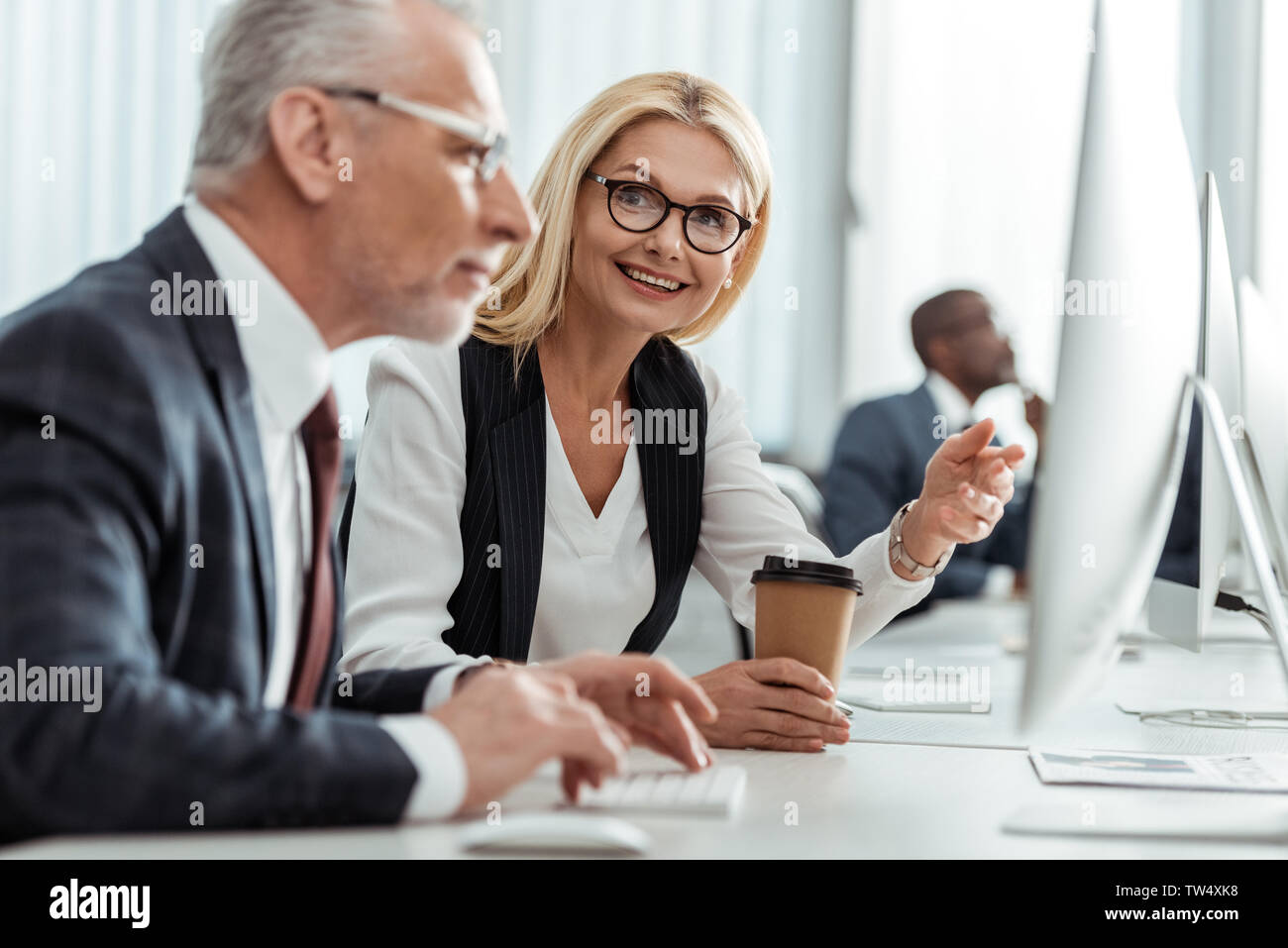 El enfoque selectivo de rubios sonrientes empresaria en gafas señalando con el dedo mientras mira compañero Foto de stock