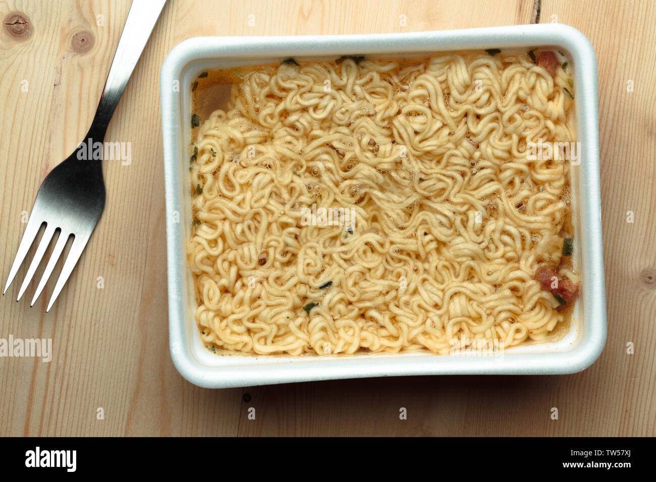 Alimentando los fideos en una mesa de madera en un plato desechable. Foto de stock