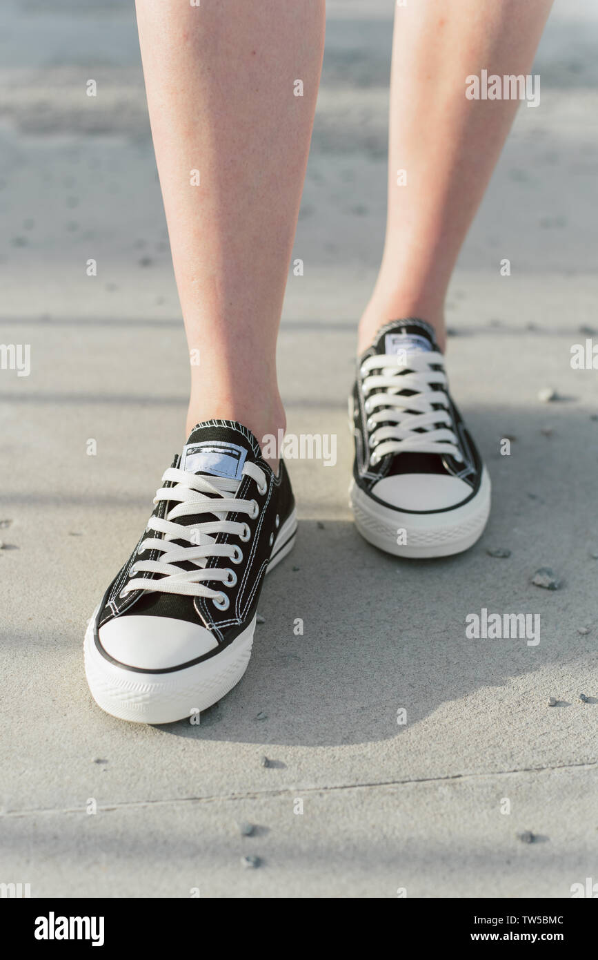Chica camina sobre el asfalto en negro sneakers. Un aspecto casual. caminando por la calle. Disparo vertical de piernas en zapatillas Fotografía de stock - Alamy