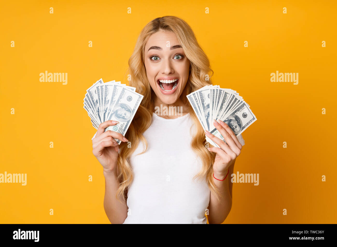 Cashback. Milenario alegre mujer sosteniendo dinero billetes sobre fondo amarillo Foto de stock